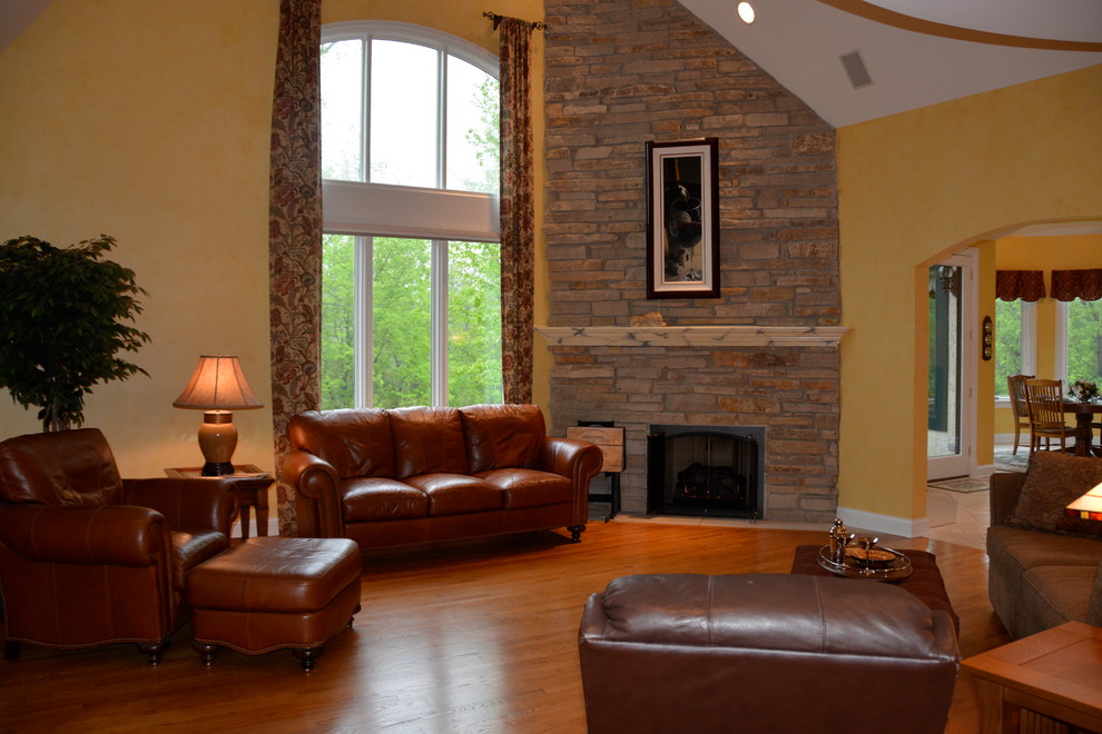 Inspiration for a large traditional open concept family room in Chicago with a corner fireplace, a stone fireplace surround, a freestanding tv, medium hardwood floors, yellow walls and brown floor.