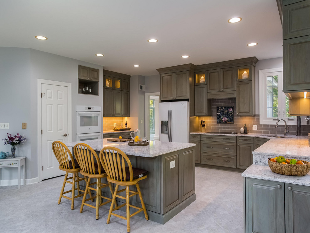 Large transitional single-wall ceramic tile and gray floor eat-in kitchen photo in DC Metro with an undermount sink, raised-panel cabinets, medium tone wood cabinets, granite countertops, brown backsplash, ceramic backsplash, white appliances, an island and white countertops