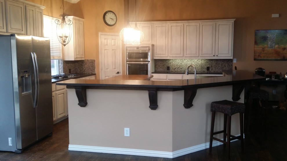 Inspiration for a large transitional brown floor open concept kitchen remodel in Dallas with an undermount sink, raised-panel cabinets, white cabinets, granite countertops, gray backsplash, stone tile backsplash, stainless steel appliances and an island