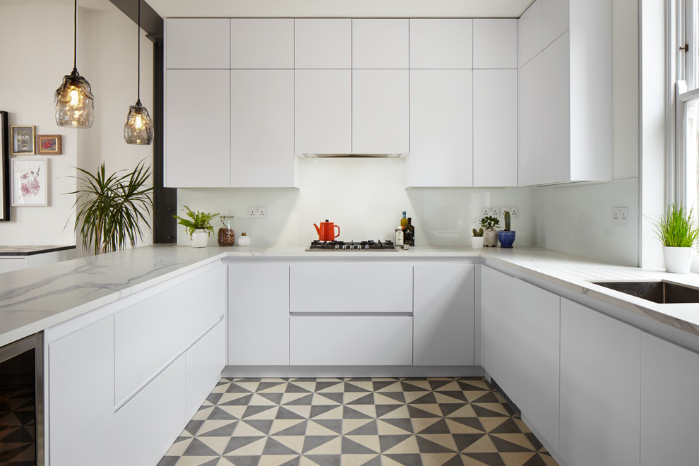 Design ideas for a large contemporary u-shaped eat-in kitchen in London with a double-bowl sink, flat-panel cabinets, white cabinets, solid surface benchtops, white splashback, glass sheet splashback, white appliances, concrete floors and a peninsula.