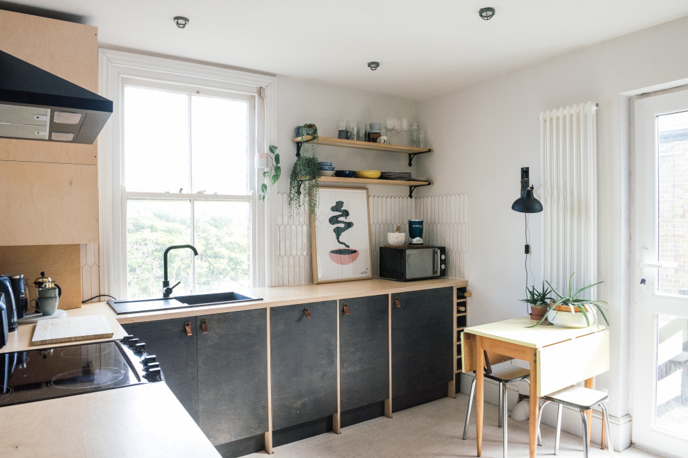 Photo of a mid-sized scandinavian l-shaped eat-in kitchen in Kent with a drop-in sink, flat-panel cabinets, black cabinets, wood benchtops, white splashback, ceramic splashback, cork floors, no island, beige floor and beige benchtop.