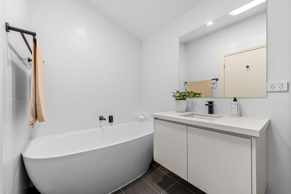 Inspiration for a small modern bathroom in Melbourne with flat-panel cabinets, white cabinets, a freestanding bath, a corner shower, a one-piece toilet, white tiles, ceramic flooring, an integrated sink, engineered stone worktops, grey floors, white worktops, a single sink and a built in vanity unit.