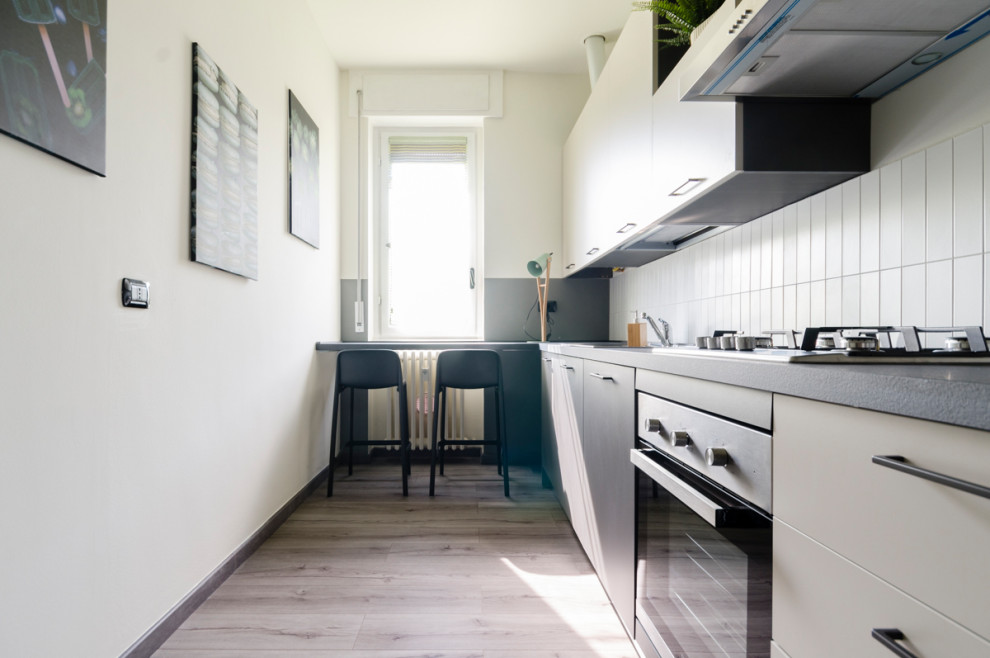 Small modern single-wall separate kitchen in Milan with a single-bowl sink, flat-panel cabinets, beige cabinets, laminate benchtops, white splashback, matchstick tile splashback, stainless steel appliances, laminate floors, grey floor and grey benchtop.