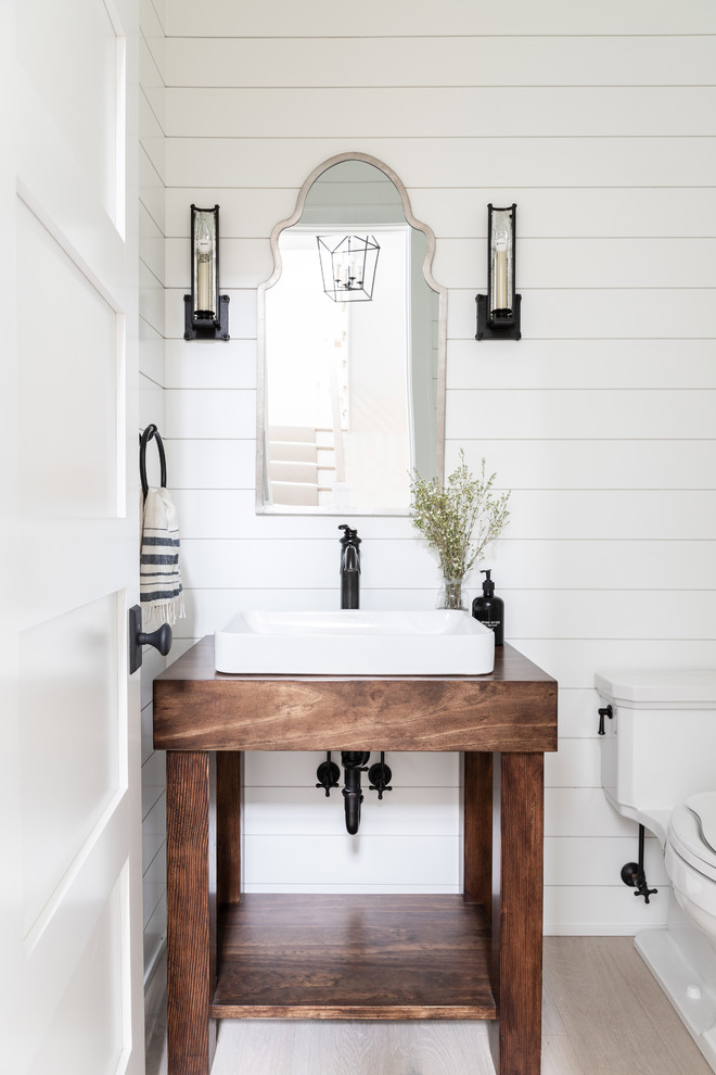 Inspiration for a small country powder room in Chicago with open cabinets, dark wood cabinets, a two-piece toilet, white walls, light hardwood floors, a vessel sink, wood benchtops, beige floor and brown benchtops.