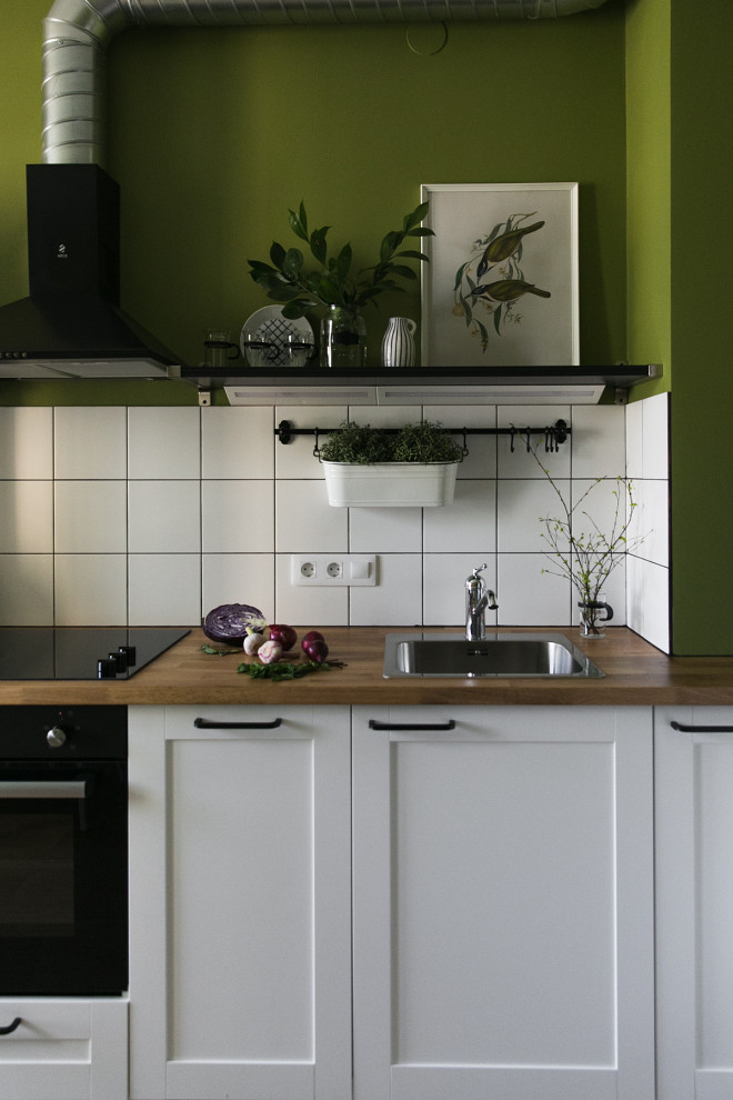 Mid-sized scandinavian l-shaped eat-in kitchen in Saint Petersburg with an undermount sink, raised-panel cabinets, white cabinets, wood benchtops, white splashback, ceramic splashback, black appliances, laminate floors, no island, brown floor and brown benchtop.