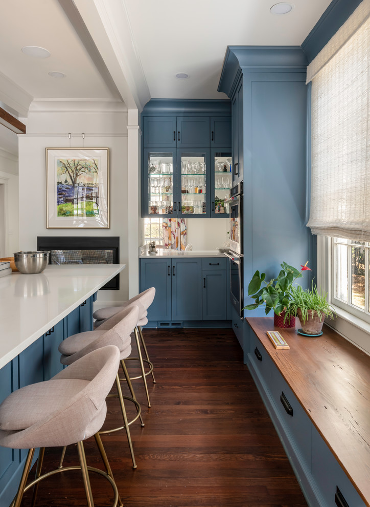 Design ideas for a mid-sized traditional galley eat-in kitchen in Atlanta with an integrated sink, flat-panel cabinets, blue cabinets, solid surface benchtops, multi-coloured splashback, ceramic splashback, stainless steel appliances, medium hardwood floors, with island, brown floor and white benchtop.