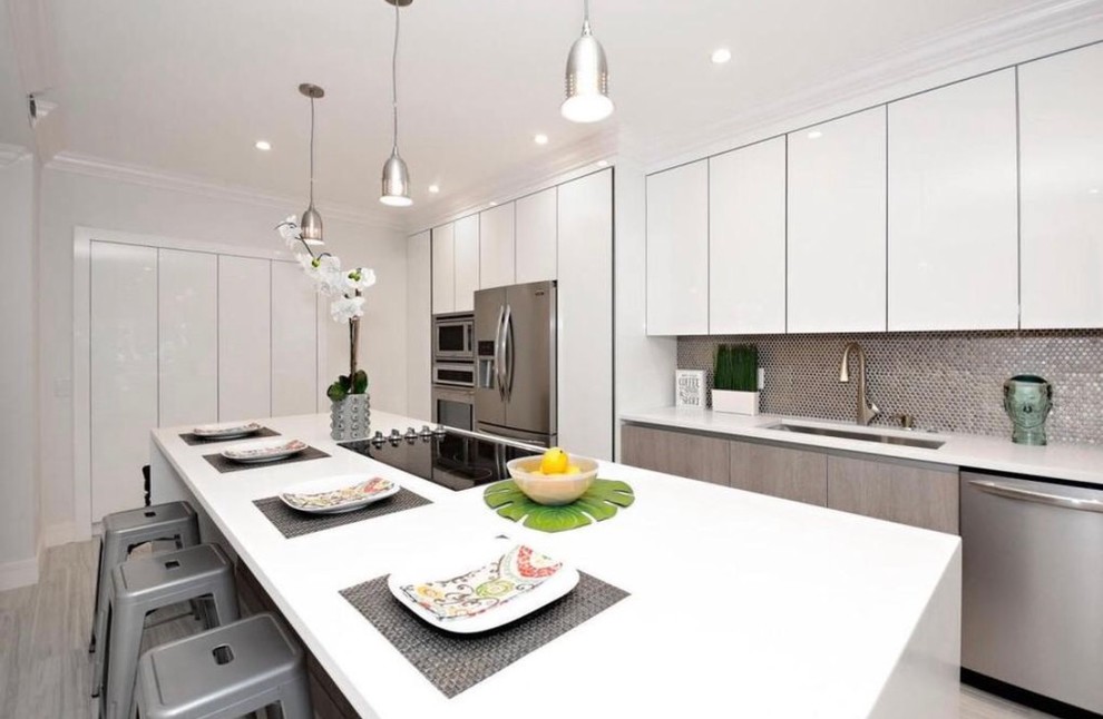 Photo of a mid-sized modern galley eat-in kitchen in Miami with a double-bowl sink, flat-panel cabinets, white cabinets, solid surface benchtops, white splashback, mosaic tile splashback, stainless steel appliances, light hardwood floors and with island.