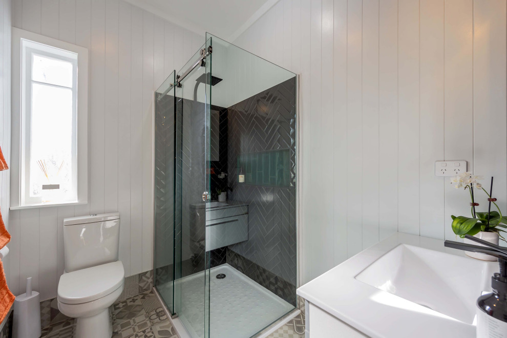 Example of a small eclectic black tile and ceramic tile porcelain tile, gray floor, single-sink and wall paneling bathroom design in Auckland with a floating vanity, flat-panel cabinets, white cabinets, a one-piece toilet, gray walls, a drop-in sink, solid surface countertops and white countertops