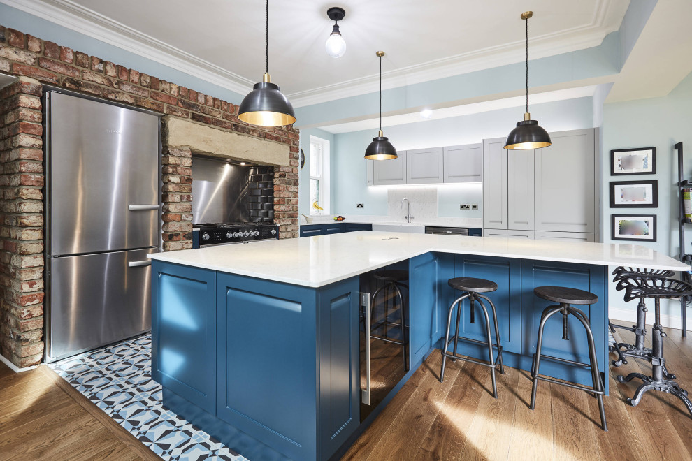 This is an example of a mid-sized l-shaped eat-in kitchen in Other with a farmhouse sink, shaker cabinets, blue cabinets, marble benchtops, white splashback, marble splashback, stainless steel appliances, porcelain floors, multiple islands, blue floor, white benchtop and coffered.