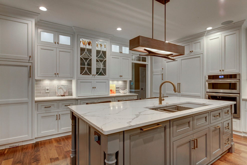 This is an example of a large transitional u-shaped open plan kitchen in Raleigh with beaded inset cabinets, white cabinets, grey splashback, panelled appliances, dark hardwood floors, with island, a triple-bowl sink, marble benchtops and subway tile splashback.