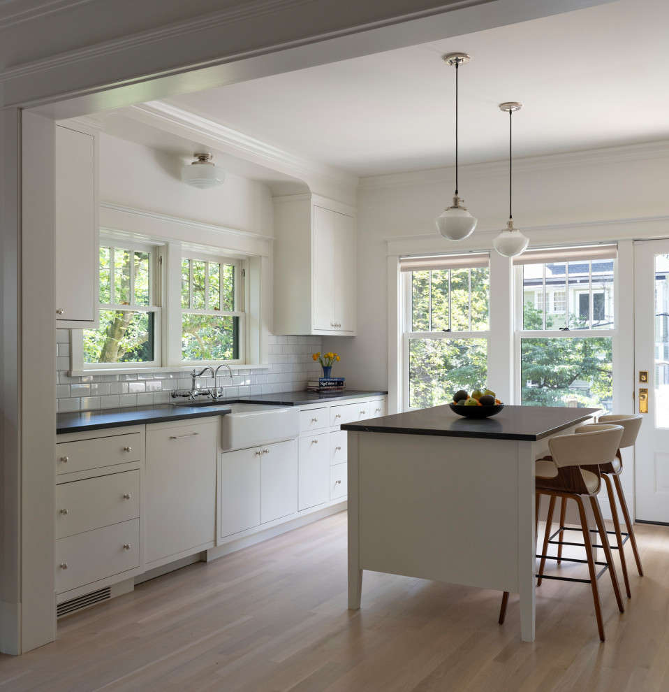 Kitchen - transitional light wood floor kitchen idea in DC Metro with a farmhouse sink, yellow cabinets, granite countertops, white backsplash, ceramic backsplash, paneled appliances, an island and black countertops