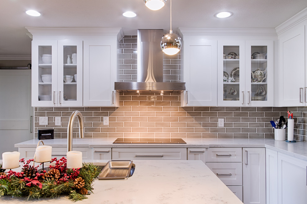 Example of a mid-sized transitional l-shaped laminate floor open concept kitchen design in Phoenix with an undermount sink, shaker cabinets, white cabinets, quartzite countertops, gray backsplash, ceramic backsplash, stainless steel appliances and an island