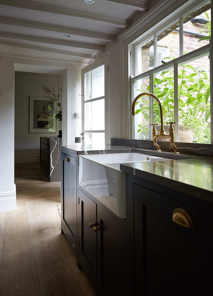 Photo of a small traditional galley kitchen pantry in London with a farmhouse sink, shaker cabinets, green cabinets, brown splashback, marble splashback, medium hardwood floors, no island, brown floor and brown benchtop.
