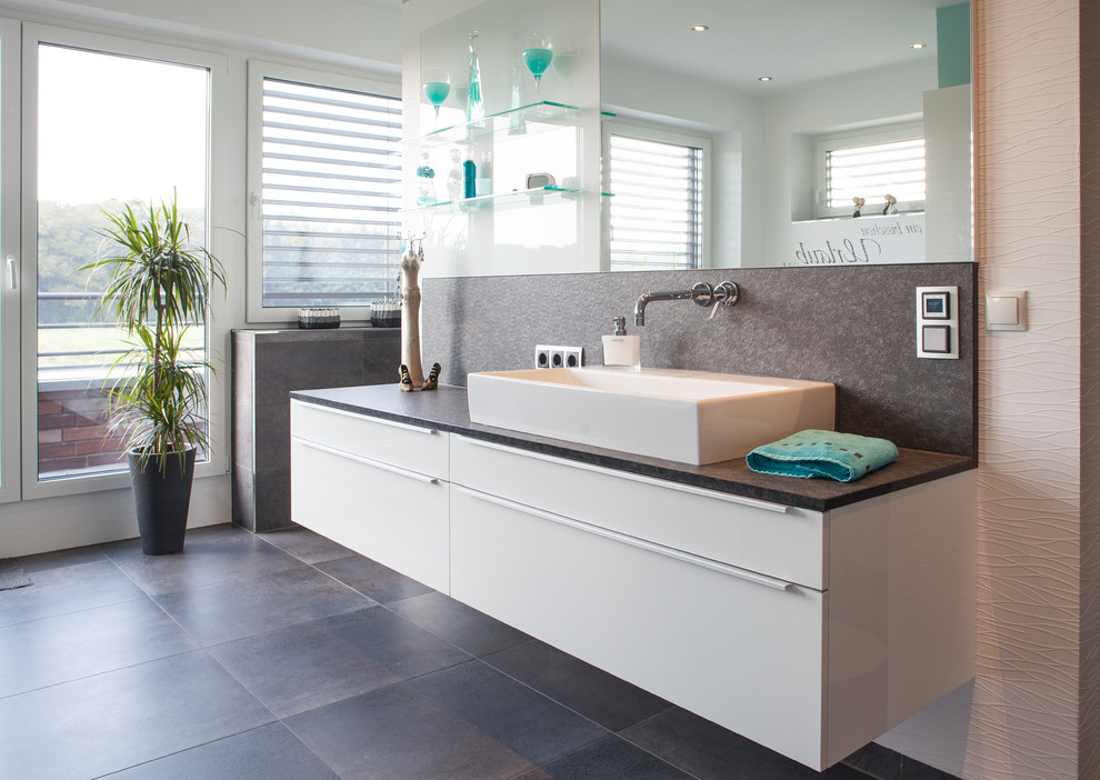 Mittelgroßes Modernes Badezimmer mit flächenbündigen Schrankfronten, weißen Schränken, grauen Fliesen, Steinplatten, weißer Wandfarbe, Schieferboden, Aufsatzwaschbecken, freistehender Badewanne, bodengleicher Dusche, Wandtoilette mit Spülkasten, Granit-Waschbecken/Waschtisch, grauem Boden und offener Dusche in Bremen