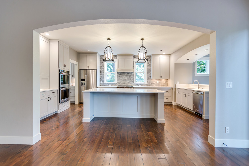 Photo of a large country u-shaped eat-in kitchen in Salt Lake City with an undermount sink, recessed-panel cabinets, grey cabinets, quartz benchtops, grey splashback, stone tile splashback, stainless steel appliances, dark hardwood floors, with island, brown floor and white benchtop.