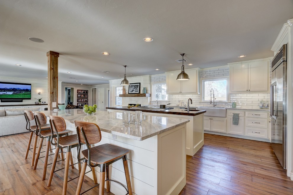 Large transitional medium tone wood floor open concept kitchen photo in Oklahoma City with a farmhouse sink, shaker cabinets, white cabinets, white backsplash, subway tile backsplash, stainless steel appliances, two islands and marble countertops