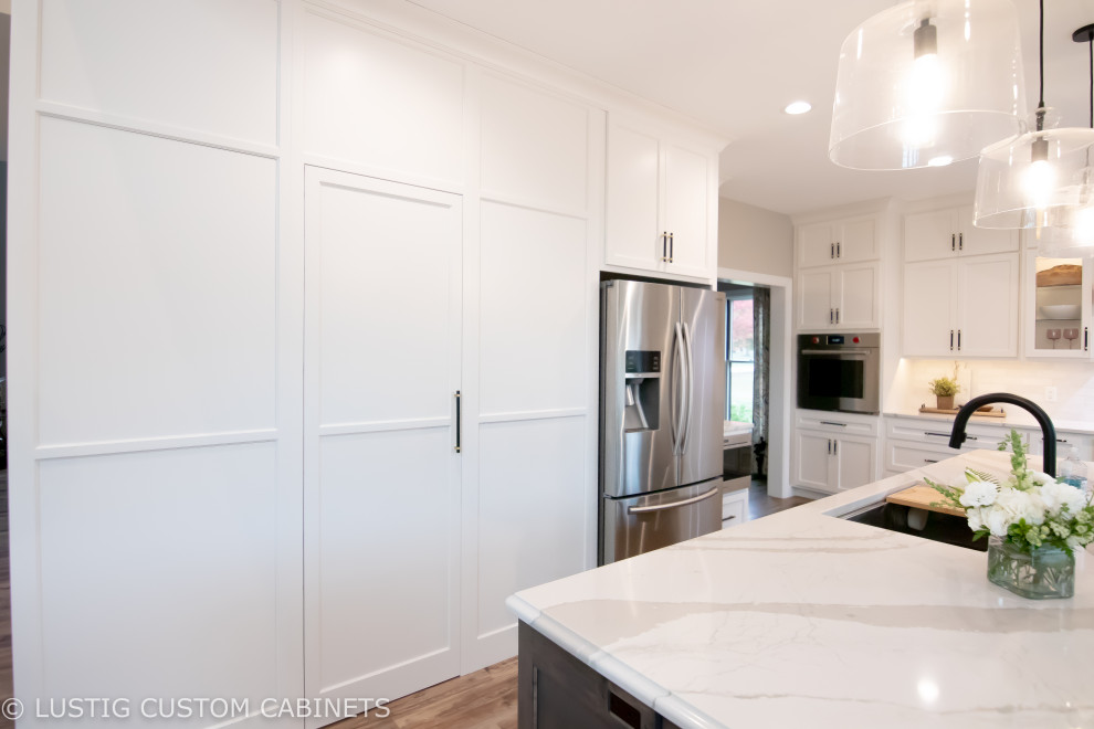 Open concept kitchen - large transitional l-shaped laminate floor and brown floor open concept kitchen idea with an undermount sink, flat-panel cabinets, white cabinets, quartz countertops, white backsplash, ceramic backsplash, stainless steel appliances, an island and white countertops