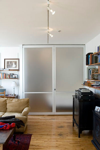 This is an example of a mid-sized modern loft-style family room in New York with a library, white walls, light hardwood floors and a freestanding tv.