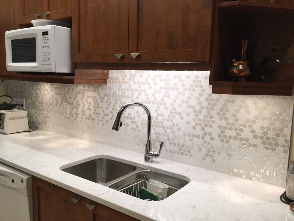 This is an example of a mid-sized transitional l-shaped kitchen in Montreal with an undermount sink, shaker cabinets, medium wood cabinets, quartz benchtops, white splashback, mosaic tile splashback, white appliances and ceramic floors.