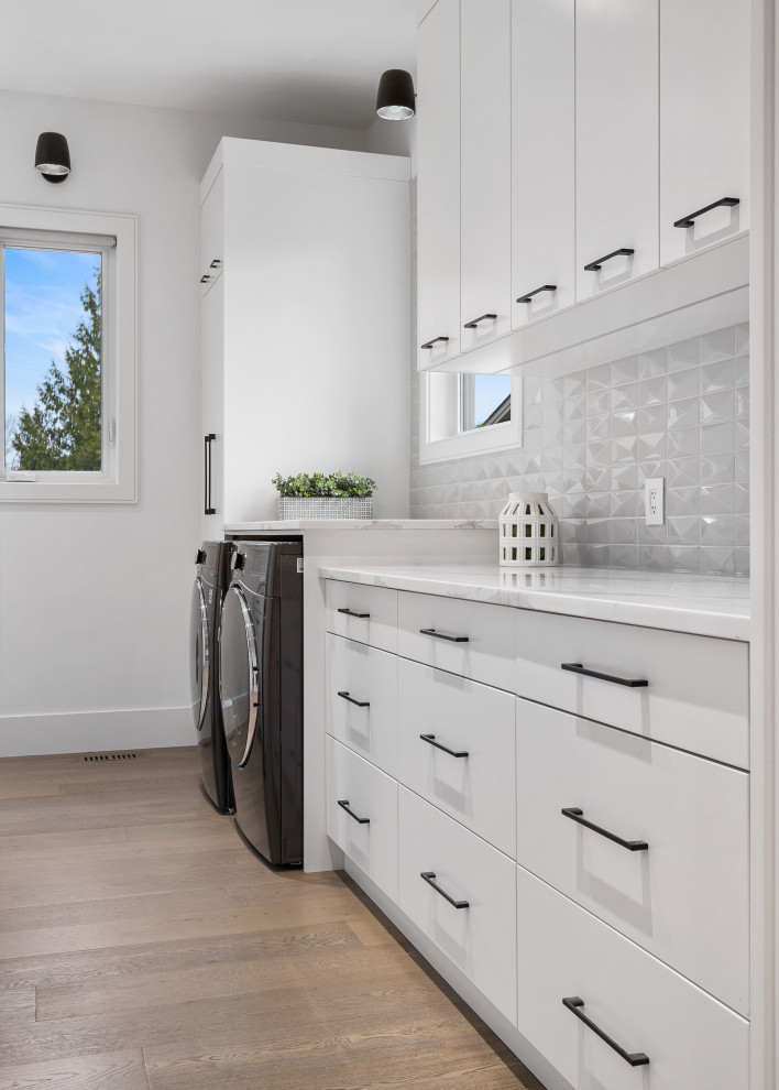 Inspiration for a mid-sized modern galley utility room in Vancouver with an undermount sink, flat-panel cabinets, white cabinets, quartzite benchtops, grey splashback, porcelain splashback, white walls, medium hardwood floors, a side-by-side washer and dryer, brown floor and multi-coloured benchtop.