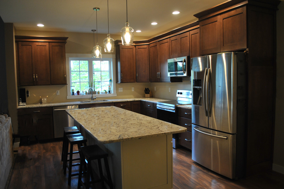 Brown floor kitchen photo with brown cabinets, stainless steel appliances, an island and beige countertops