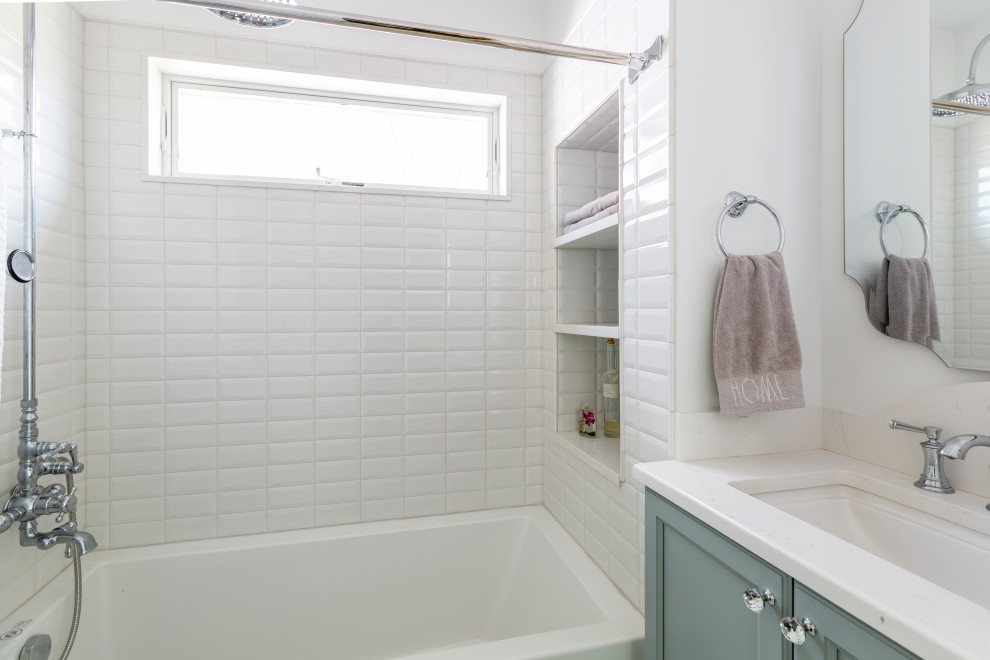 Photo of a small classic ensuite bathroom in New York with shaker cabinets, blue cabinets, an alcove bath, a shower/bath combination, a two-piece toilet, white tiles, porcelain tiles, white walls, mosaic tile flooring, a submerged sink, engineered stone worktops, white floors, a shower curtain, white worktops, a wall niche, a single sink and a built in vanity unit.