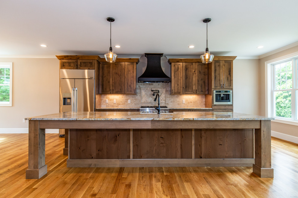 Design ideas for a country eat-in kitchen in Providence with a farmhouse sink, shaker cabinets, brown cabinets, granite benchtops, beige splashback, marble splashback, stainless steel appliances, medium hardwood floors, with island, brown floor and grey benchtop.