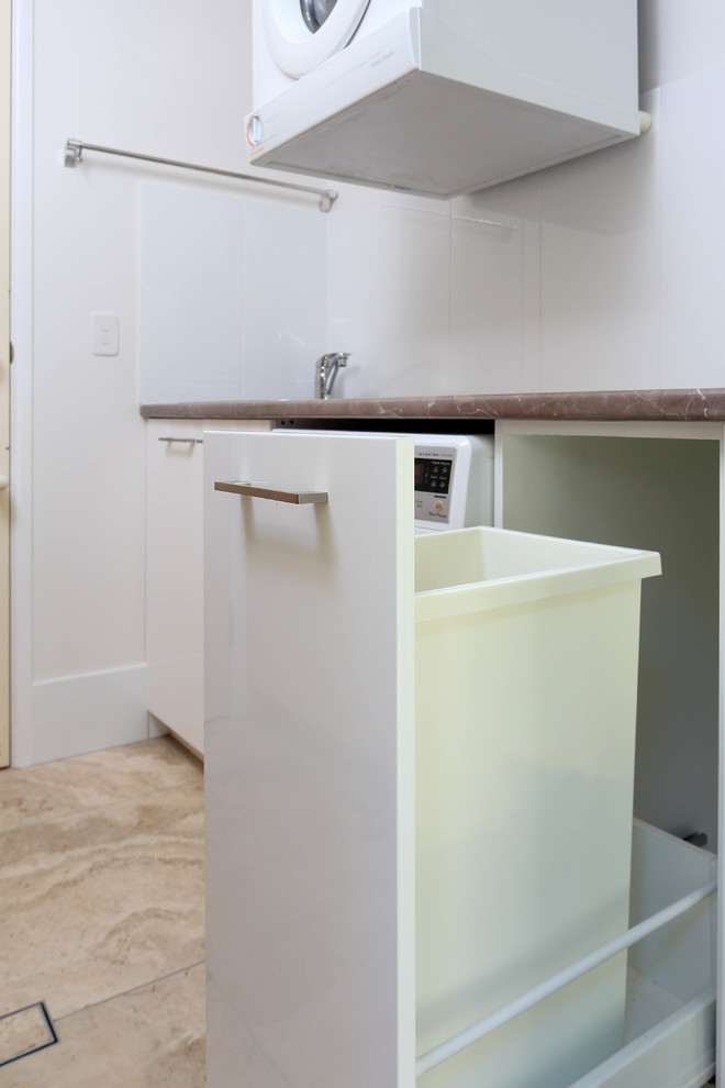 Photo of a small modern l-shaped laundry cupboard in Brisbane with an undermount sink, flat-panel cabinets, white cabinets, quartz benchtops, grey walls, porcelain floors, an integrated washer and dryer, white floor and grey benchtop.