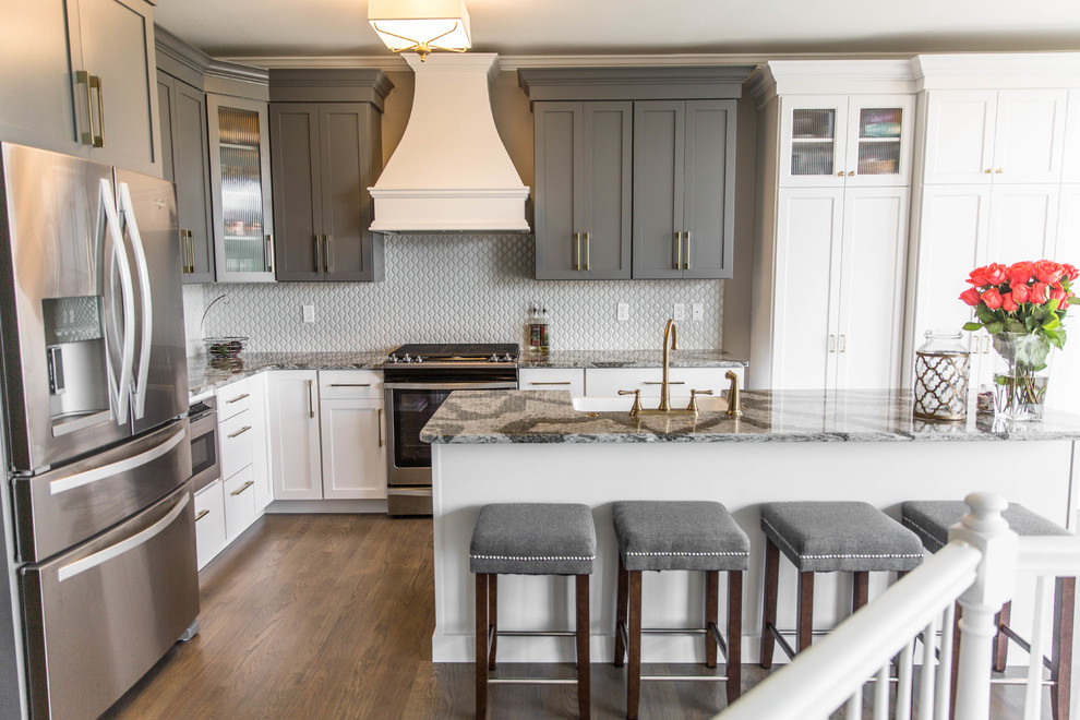 Example of a mid-sized transitional l-shaped medium tone wood floor eat-in kitchen design in Philadelphia with a farmhouse sink, shaker cabinets, white cabinets, quartz countertops, gray backsplash, porcelain backsplash, stainless steel appliances and an island