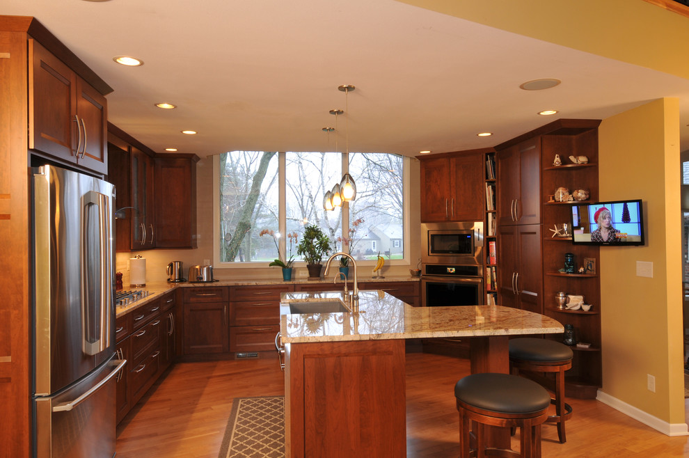 This is an example of a large modern u-shaped eat-in kitchen in Milwaukee with a farmhouse sink, recessed-panel cabinets, dark wood cabinets, granite benchtops, beige splashback, porcelain splashback, stainless steel appliances and with island.