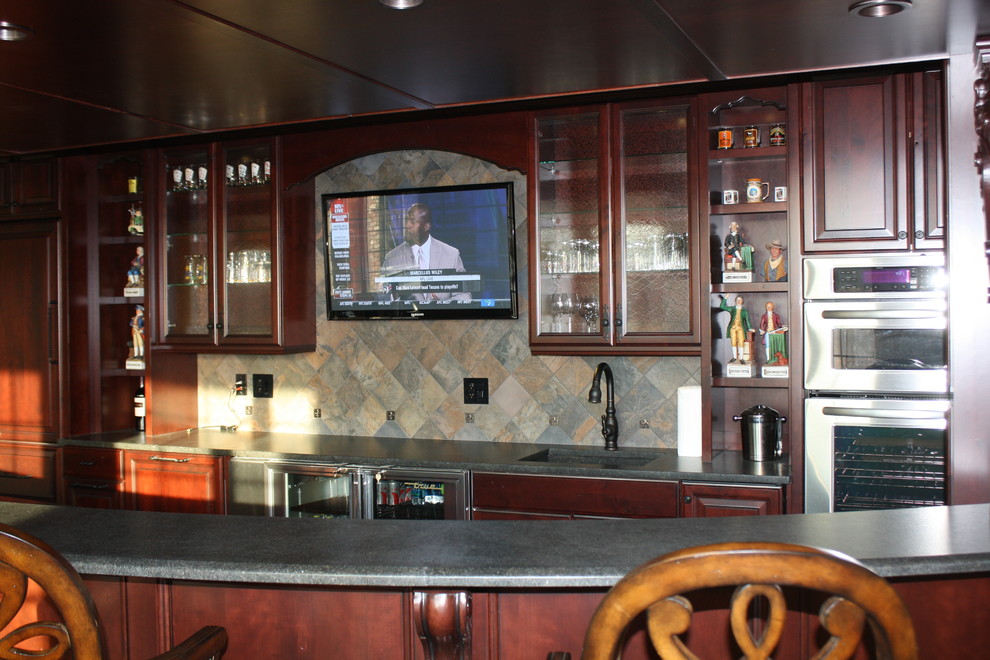 Design ideas for a large arts and crafts galley seated home bar in Chicago with an integrated sink, glass-front cabinets, dark wood cabinets, granite benchtops, multi-coloured splashback and stone tile splashback.