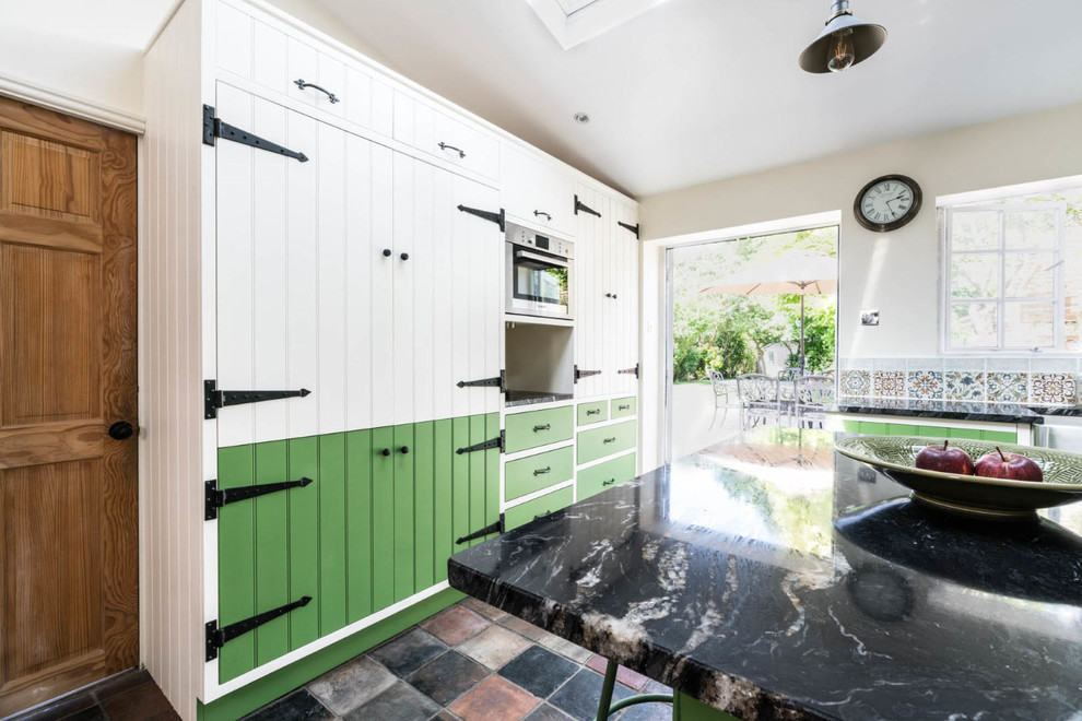 This is an example of a small country l-shaped eat-in kitchen in Essex with a farmhouse sink, green cabinets, granite benchtops, multi-coloured splashback, mosaic tile splashback, panelled appliances, porcelain floors, with island, multi-coloured floor and black benchtop.