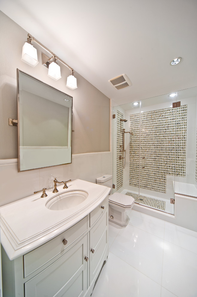 This is an example of a beach style master bathroom in New York with an undermount sink, shaker cabinets, white cabinets, an alcove shower, a two-piece toilet, multi-coloured tile, mosaic tile and beige walls.