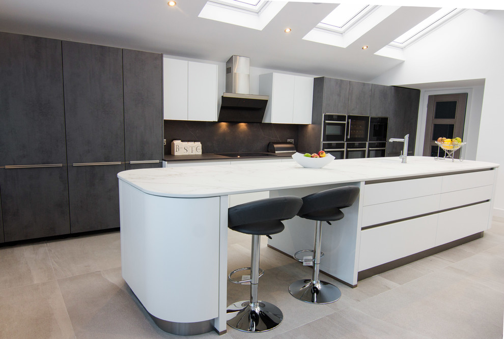 This is an example of a contemporary eat-in kitchen in Other with a drop-in sink, flat-panel cabinets, white cabinets, solid surface benchtops, black splashback, stone slab splashback, black appliances, porcelain floors, with island, beige floor and white benchtop.