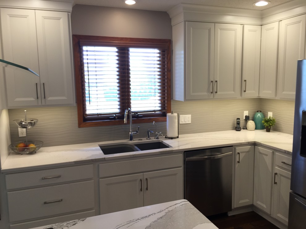 Example of a large transitional l-shaped dark wood floor home design design with an undermount sink, flat-panel cabinets, white cabinets, quartz countertops, white backsplash, ceramic backsplash, stainless steel appliances and an island