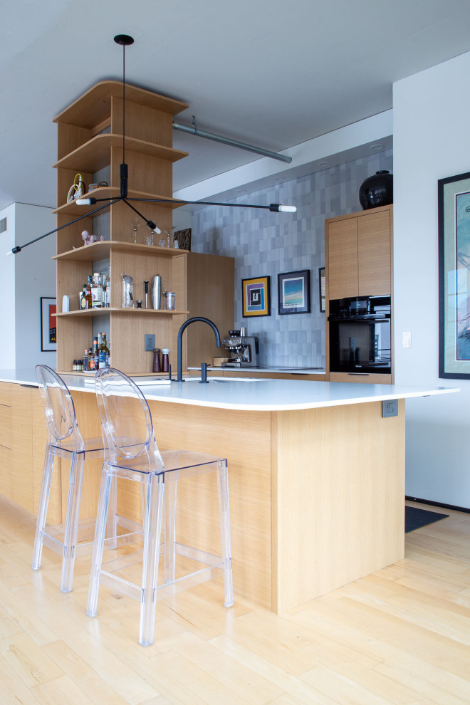 Bild på ett mellanstort funkis vit vitt kök, med släta luckor, skåp i ljust trä, bänkskiva i kvarts, grått stänkskydd, stänkskydd i keramik, integrerade vitvaror, ljust trägolv och en köksö