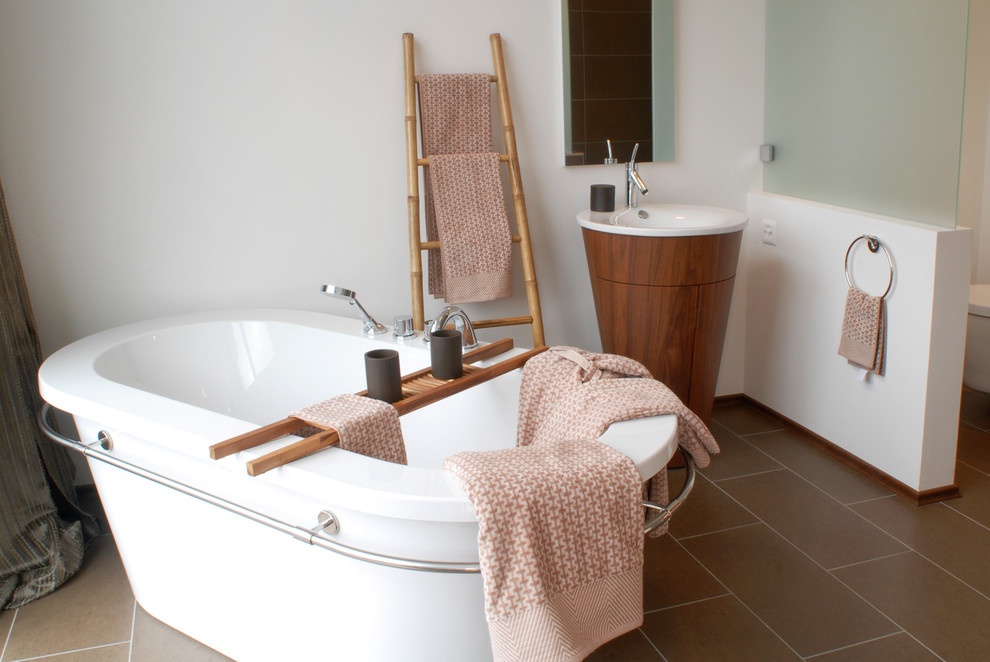 Photo of a mid-sized asian master bathroom in Berlin with flat-panel cabinets, dark wood cabinets, a freestanding tub, a wall-mount toilet, white walls, a pedestal sink and brown floor.