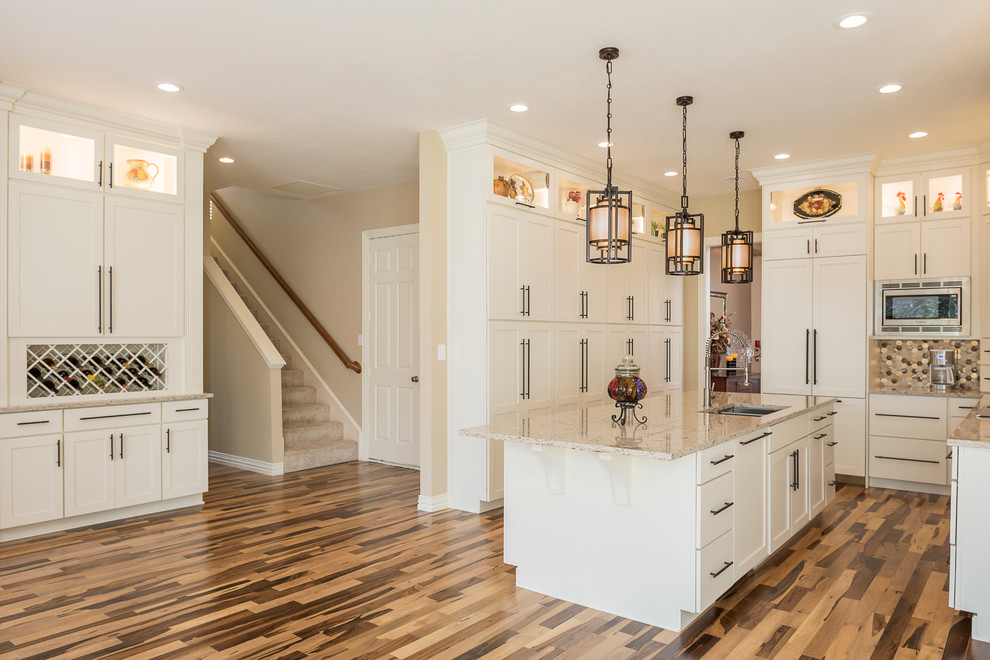 Inspiration for a mid-sized transitional galley light wood floor kitchen pantry remodel in Dallas with an undermount sink, shaker cabinets, white cabinets, granite countertops, beige backsplash, ceramic backsplash, stainless steel appliances and an island