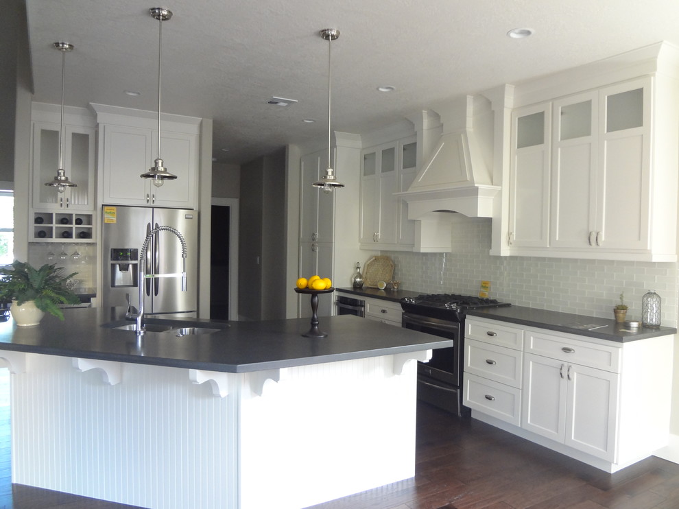 This is an example of a mid-sized arts and crafts l-shaped eat-in kitchen in Portland with a double-bowl sink, shaker cabinets, white cabinets, concrete benchtops, white splashback, glass tile splashback, stainless steel appliances, dark hardwood floors and with island.
