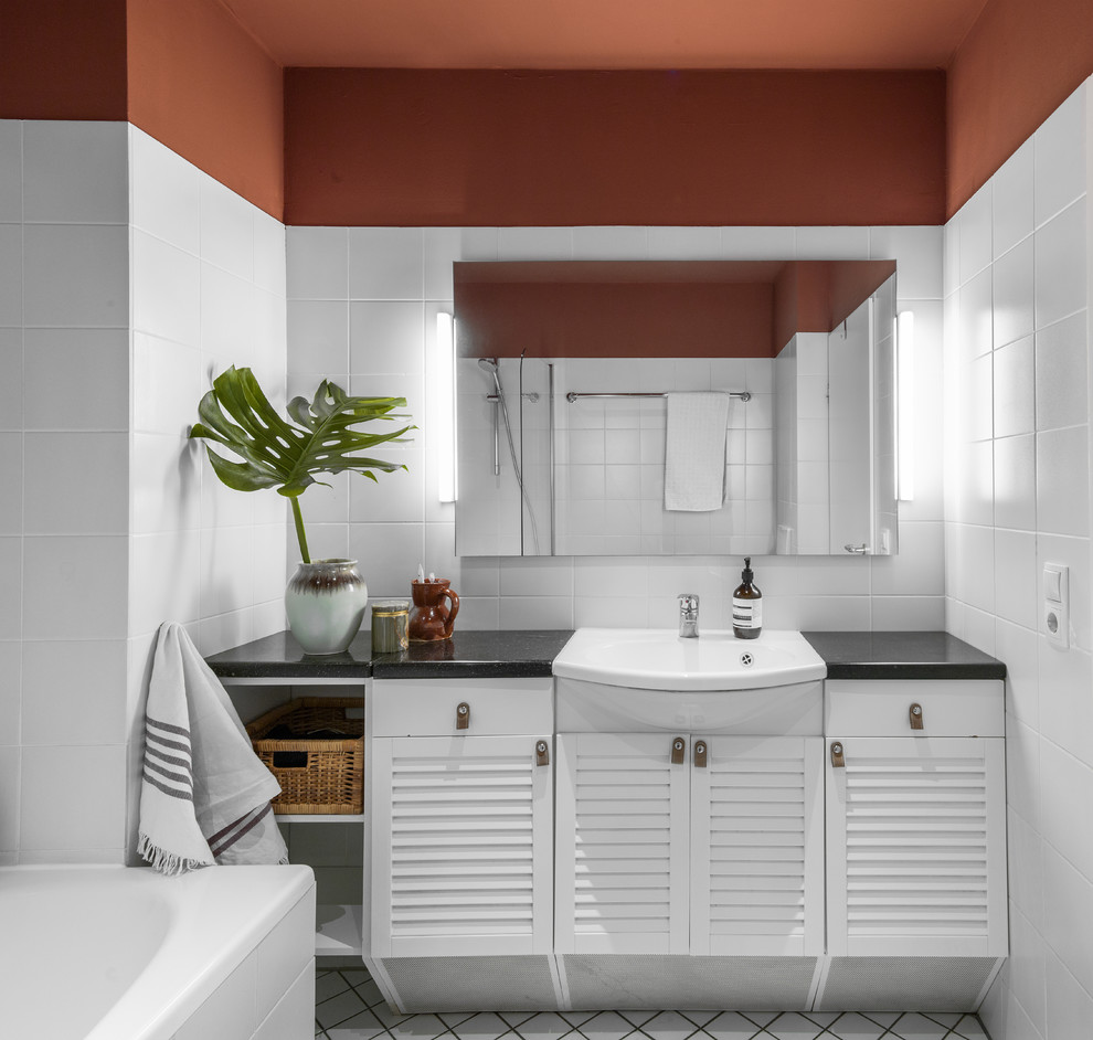 This is an example of a contemporary 3/4 bathroom in Hamburg with red walls, granite benchtops, black benchtops, louvered cabinets, white cabinets, a drop-in tub, white tile, porcelain tile, a vessel sink and white floor.
