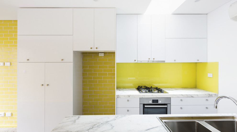 Design ideas for a small contemporary galley eat-in kitchen in Sydney with a double-bowl sink, raised-panel cabinets, white cabinets, marble benchtops, yellow splashback, glass sheet splashback, white appliances, concrete floors and with island.