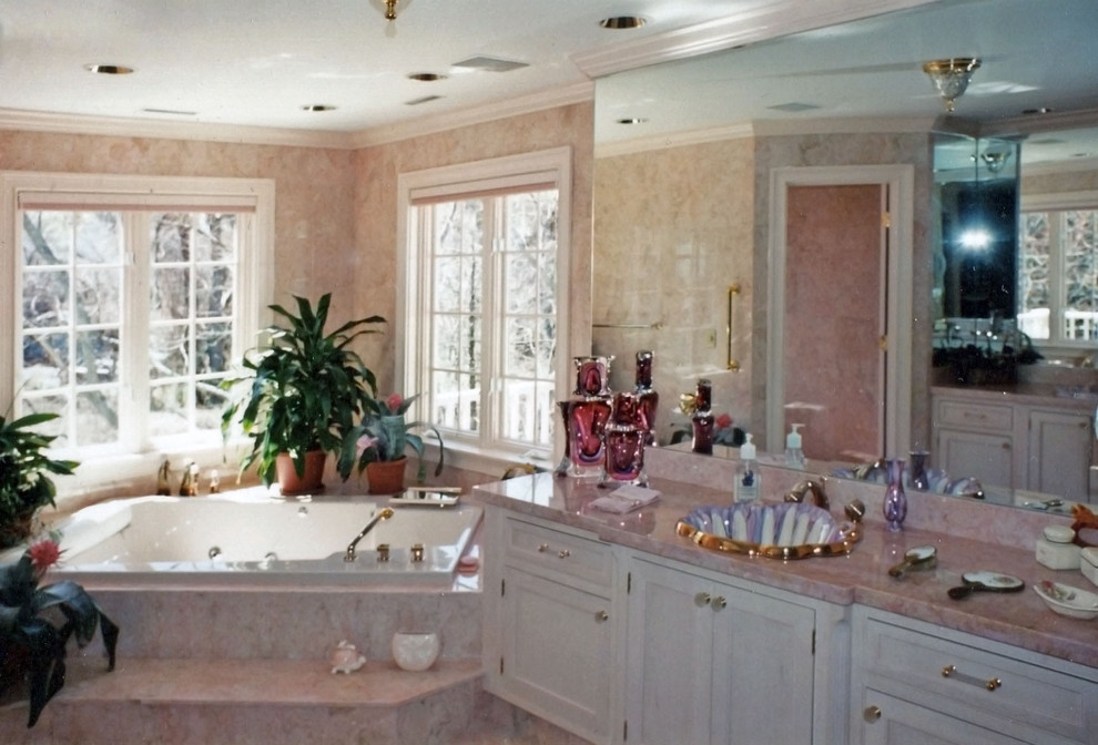 Photo of a large traditional master bathroom in Boston with recessed-panel cabinets, brown cabinets, beige walls, an undermount sink, marble benchtops, a drop-in tub, marble floors, pink floor, an alcove shower and a hinged shower door.