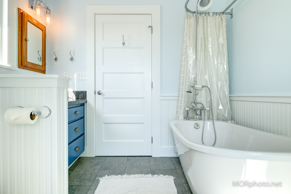 Photo of a mid-sized country bathroom in Portland with shaker cabinets, blue cabinets, a freestanding tub, a shower/bathtub combo, a bidet, blue walls, vinyl floors, an undermount sink, granite benchtops, grey floor, a shower curtain, black benchtops, a laundry, a single vanity, a built-in vanity and decorative wall panelling.