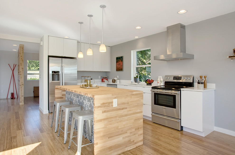 Trendy l-shaped kitchen photo in Seattle with flat-panel cabinets, white cabinets, wood countertops, white backsplash and stainless steel appliances