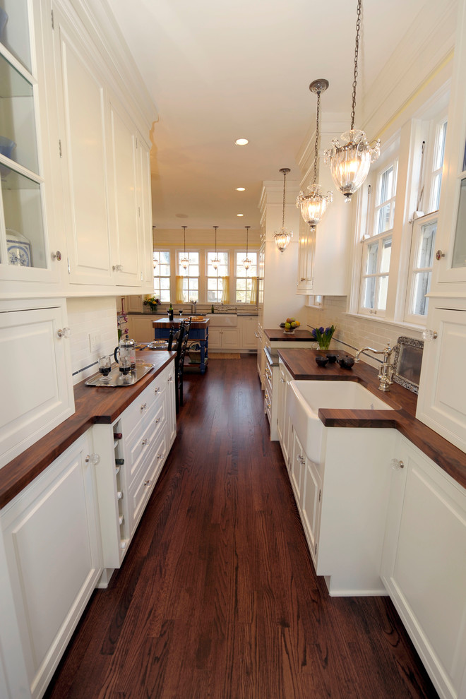 This is an example of a mid-sized traditional galley separate kitchen in Chicago with a farmhouse sink, raised-panel cabinets, white cabinets, white splashback, subway tile splashback, stainless steel appliances, medium hardwood floors and with island.