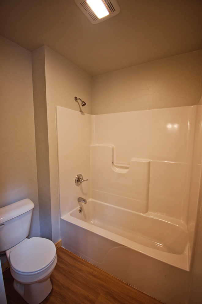 Example of a mid-sized mountain style master beige tile medium tone wood floor and brown floor tub/shower combo design with recessed-panel cabinets, dark wood cabinets, a two-piece toilet, beige walls, a drop-in sink, laminate countertops and brown countertops
