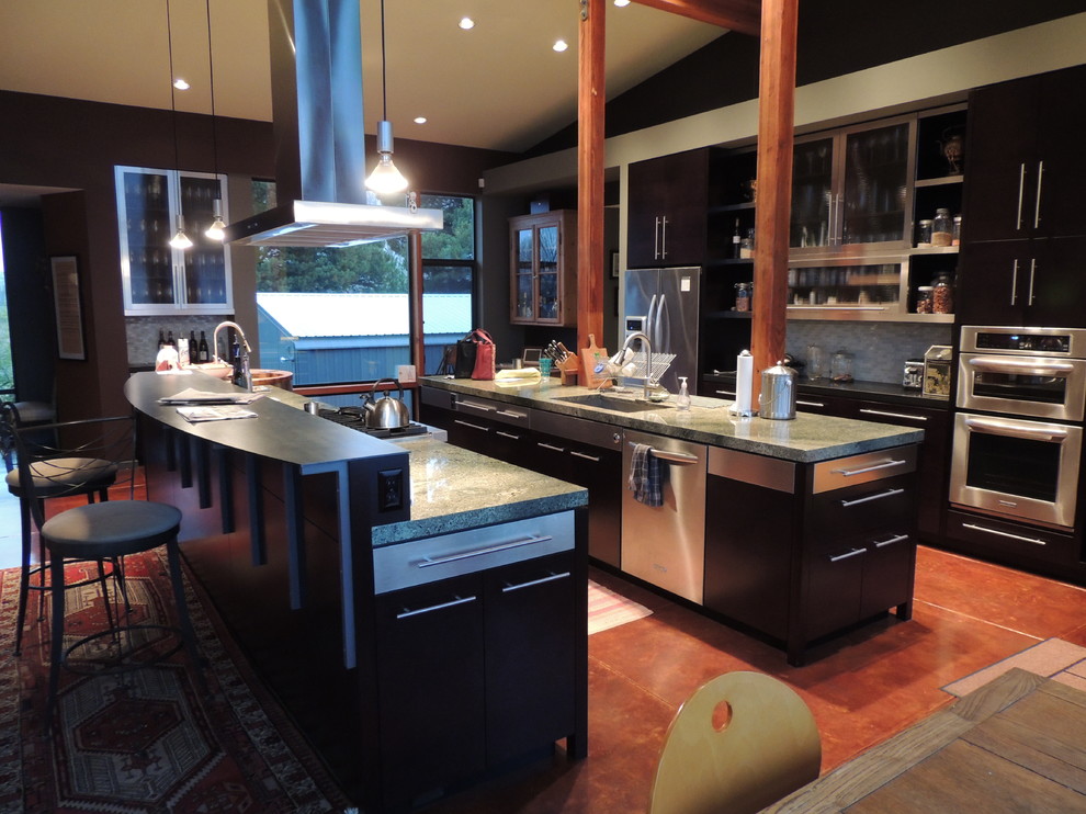 Inspiration for a large modern galley open plan kitchen in Portland with flat-panel cabinets, dark wood cabinets, granite benchtops, glass tile splashback, stainless steel appliances, concrete floors, multiple islands, white splashback, red floor, green benchtop and vaulted.