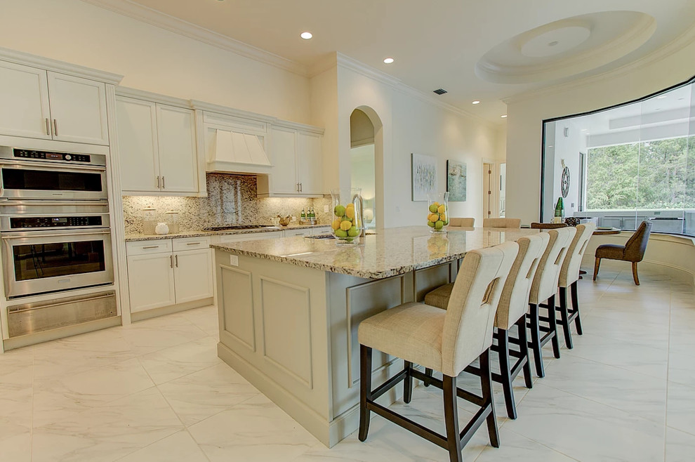 Inspiration for a large transitional l-shaped eat-in kitchen in Miami with an undermount sink, shaker cabinets, white cabinets, granite benchtops, beige splashback, stone slab splashback, stainless steel appliances, marble floors, with island and white floor.
