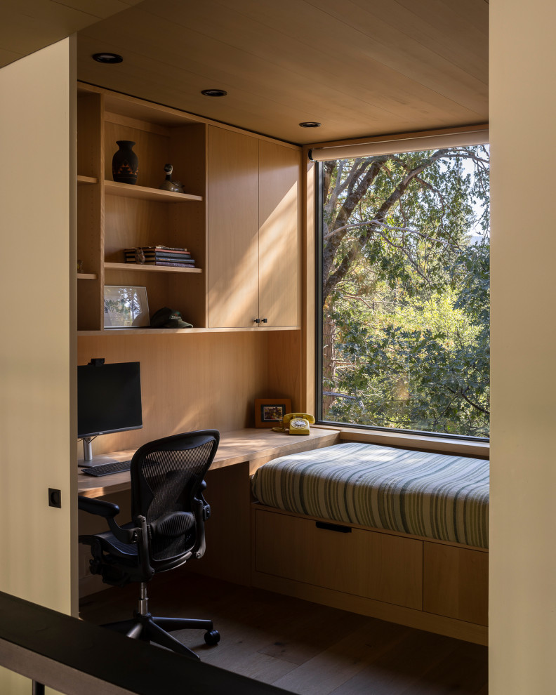 This is an example of a modern home office in Seattle with medium hardwood floors, a built-in desk, brown floor and wood.