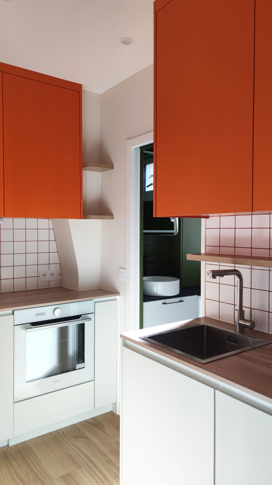 Inspiration för mellanstora moderna linjära brunt kök, med en enkel diskho, luckor med profilerade fronter, orange skåp, laminatbänkskiva, vitt stänkskydd, stänkskydd i keramik, vita vitvaror, ljust trägolv och flera köksöar